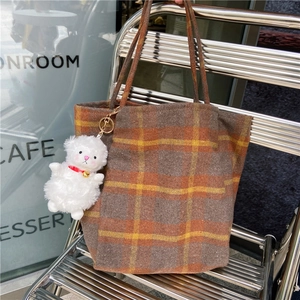 Detail view of plaid wool tote bag with plush charm on an industrial metal chair
