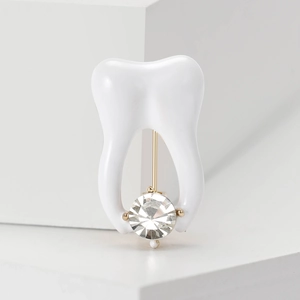 Macro detail of tooth brooch with white enamel, large sparkling crystal and golden plating
