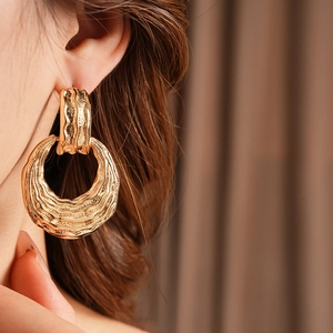 Close-up of model wearing textured gold wavy hoop earrings with a metallic finish