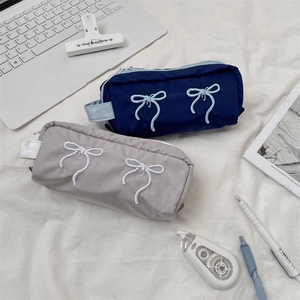Flat lay of embroidered bow pencil cases in navy and gray on a minimalist desk