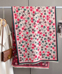 Close-up of floral print scarf with green border and tassels hanging on a hanger