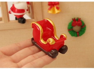 Close-up of a miniature red resin Christmas sleigh with gold trim held by a hand