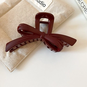 Macro detail of glossy wine red bow hair claw clip on soft beige fabric background