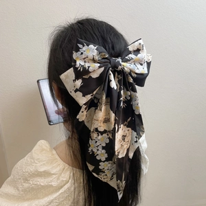 Black satin bow hair clip with camellia floral patterns worn on elegant long wavy hair