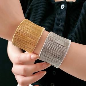 Dettaglio di bracciali a polsino intrecciati in oro e argento indossati sul polso femminile