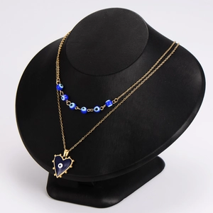 Double-layered gold necklace featuring blue evil eye beads and heart pendant on black bust
