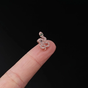 Macro shot of rose gold snake ear stud with white zircons and green gem eyes on fingertip