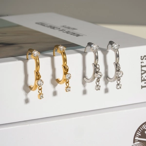 Close-up of gold and silver C-shaped hoop earrings with sparkling crystal pendants