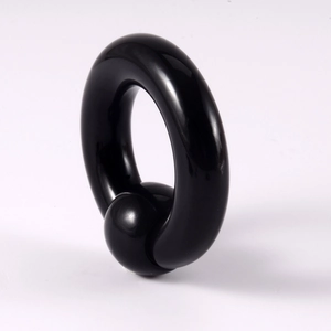 Close-up of a large black acrylic captive bead ring for body piercing on white background