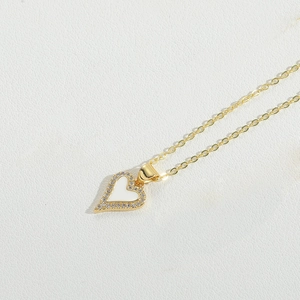 Macro shot of gold heart pendant necklace with white enamel inlay and sparkling crystals