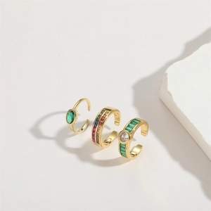 Three gold rings featuring emerald and multi-colored zircons on a white marble background
