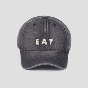 Macro detail of EAT embroidery on washed grey denim baseball cap with vintage texture