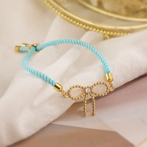 Detail of blue braided rope bracelet with golden bow charm and sparkling zircon