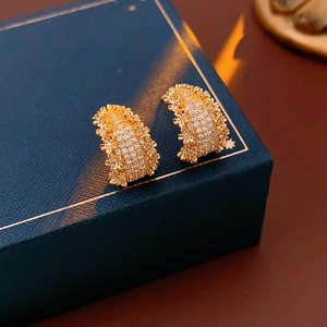 Détail de boucles d'oreilles dorées en forme de C serties de zircons et texture florale