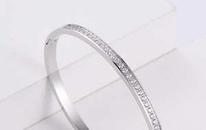 Detailed close-up of a silver rhinestone-inlaid open bangle on a minimalist white stand