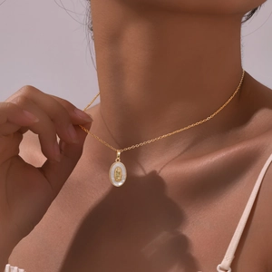 Detail view of oval gold necklace with Virgin Mary relief on white shell on a model's neck