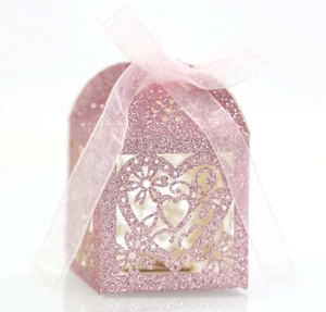 Gros plan sur boîte à bonbons rose pailletée avec motifs cœur découpés et ruban de soie