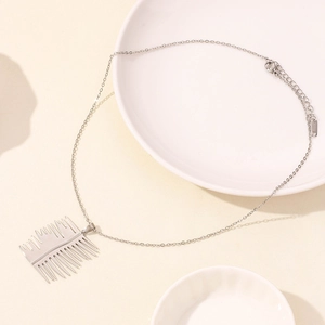 Detailed view of a silver-tone comb pendant on a minimalist stainless steel chain