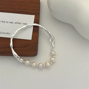 Macro shot of silver wave branch bracelet with natural baroque pearls on wood stand