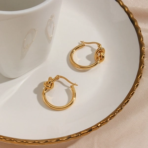Close-up of golden knotted hoop earrings in a ceramic tray with silk background