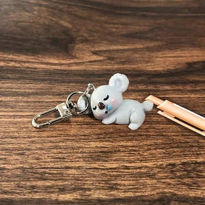 Sleeping koala animal keychain in grey resin hanging on a dark wood background
