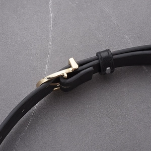 Close-up of black leather belt with a minimalist golden T-shaped buckle on marble