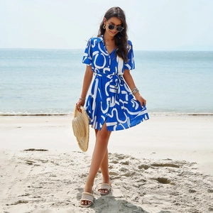 Elegant blue short sleeve dress with white geometric prints and a waist belt on a beach