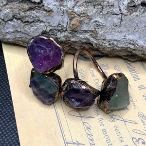 Detail of vintage copper rings with raw amethyst and green fluorite on bark texture