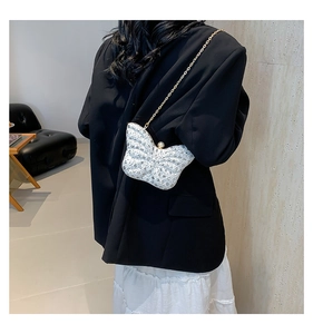Sac bandoulière blanc en forme de papillon avec chaîne dorée porté par un mannequin