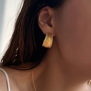 Golden hammer textured wide hoop earring with cubic zirconia studs on female model