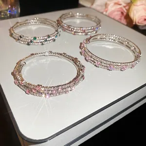 Three-layer stacked zircon bracelets with pink and green stones on a luxury display