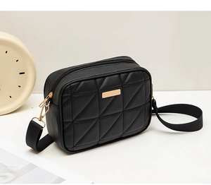 Close-up of black quilted camera bag with triangle metal detail and wide strap