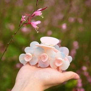 Détail d'une pince à cheveux fleurie aux pétales nacrés rose et bleu clair en acétate