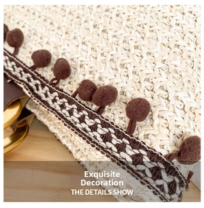 Close-up of woven straw bag texture with brown pom-pom and geometric patterned trim detail