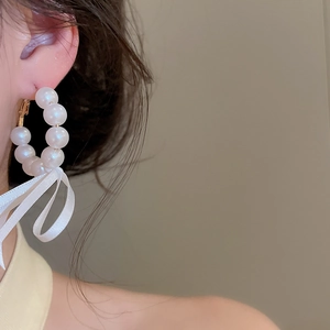 Close-up of elegant French style pearl hoop earrings with a white ribbon bow detail