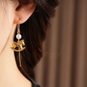 Detail of golden rocking horse earrings with long tassels and pearls on model
