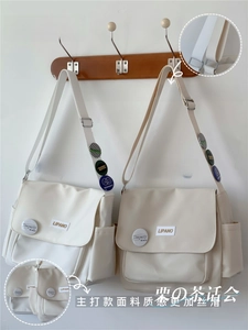 Detail of cream canvas messenger bag showing logo patch and colorful badges on shoulder strap