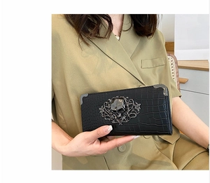 Detail of black crocodile embossed clutch featuring a decorative metal skull and corners