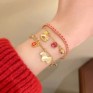 Close-up of three gold bracelets set with red cord and bear charms on a knit sleeve