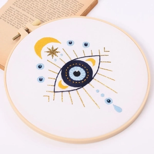 DIY evil eye embroidery kit in a round wooden hoop with blue and gold threads