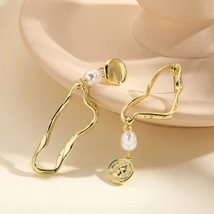 Detail of asymmetrical gold earrings featuring baroque pearls and vintage coin charms
