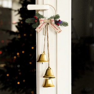 Christmas hanging ornament with three golden bells, pine branches, and berries on a door