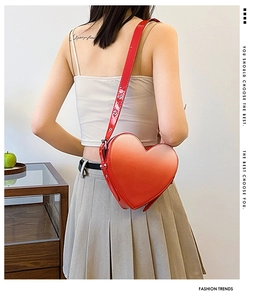Détail d'un sac bandoulière rouge brillant en forme de cœur avec une sangle réglable