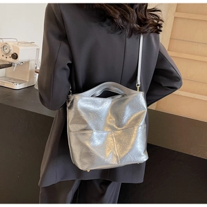 Close-up of silver tote bag with pleated texture shown on shoulder of model in black suit