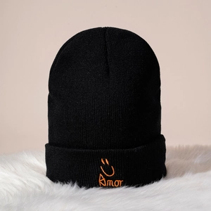 Gros plan du bonnet en tricot noir avec texte Amor orange et broderie de visage souriant