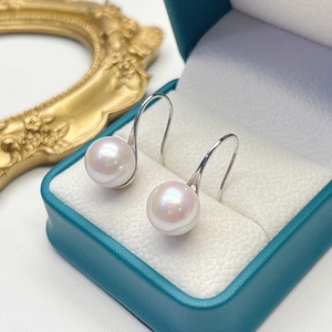 Close-up of elegant freshwater pearl earrings on silver hooks in a teal jewelry box