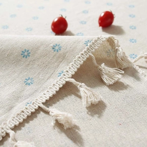 Detail of linen tablecloth with blue floral pattern and elegant beige fringe edges