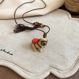 Close-up of pug pendant with red backpack and bone bead on brown adjustable wax rope