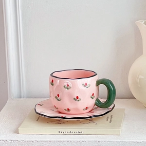 Detail of pink ceramic coffee cup and saucer set with hand-painted strawberry motifs