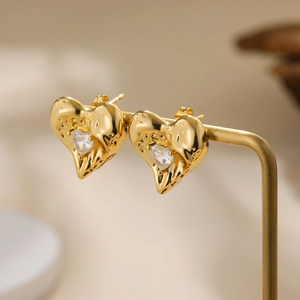 Macro shot of a gold heart stud earring with a central zircon on a metal jewelry stand